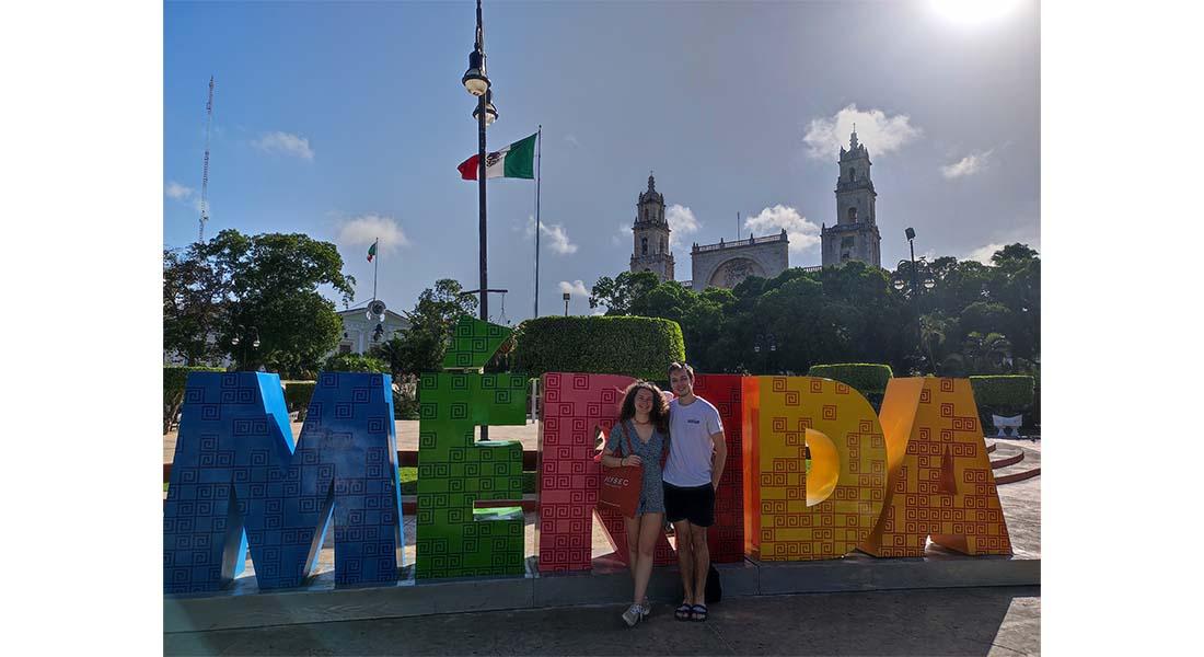 Une femme et un homme devant enseigne de la ville Merida au Mexique